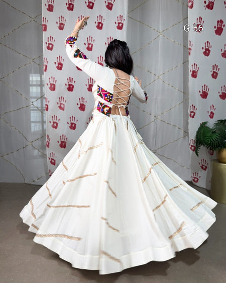 Woman in a white dress with gold patterns dancing in front of a curtain with red handprints.
