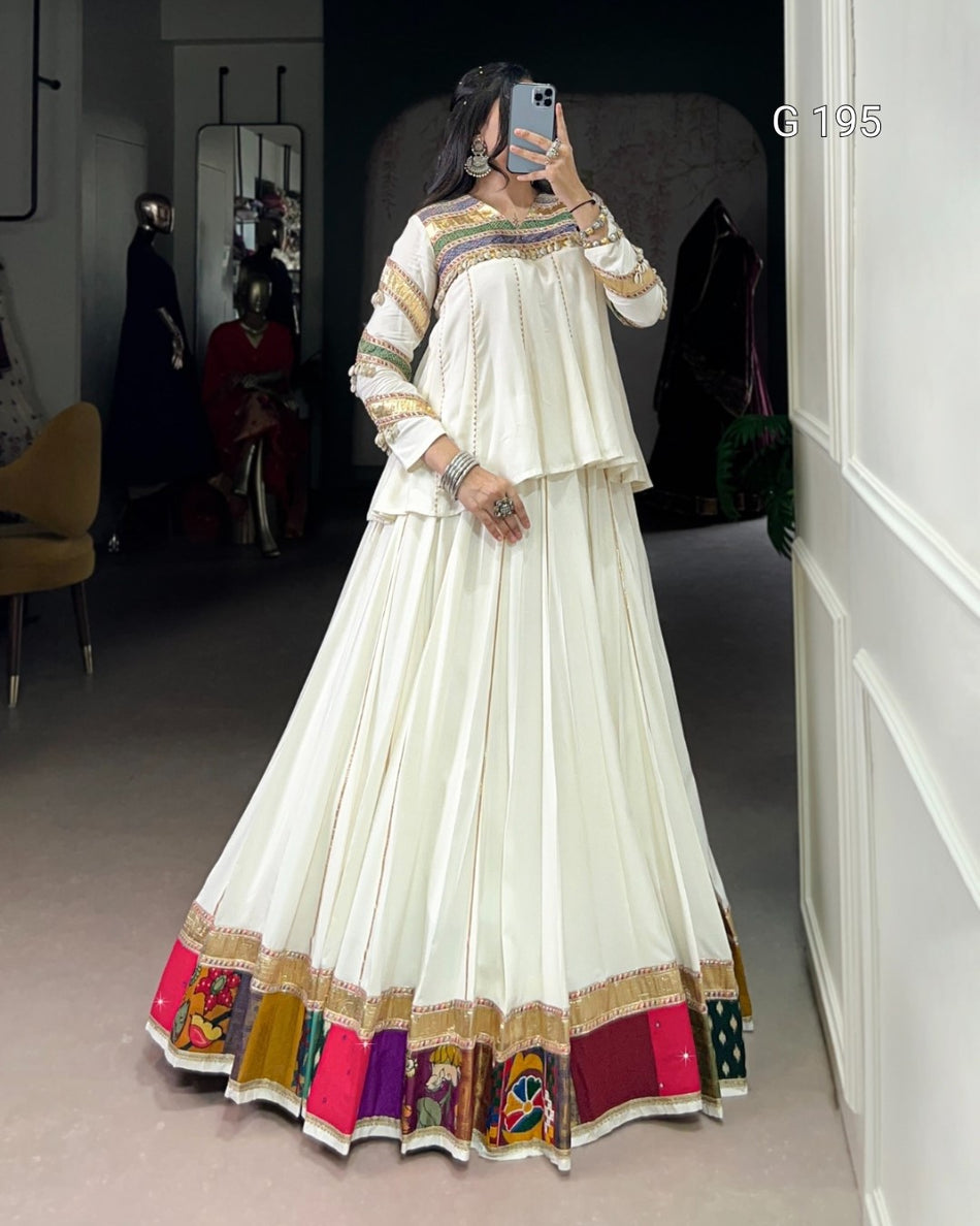 Person wearing a long, white dress with colorful patterns in a room.