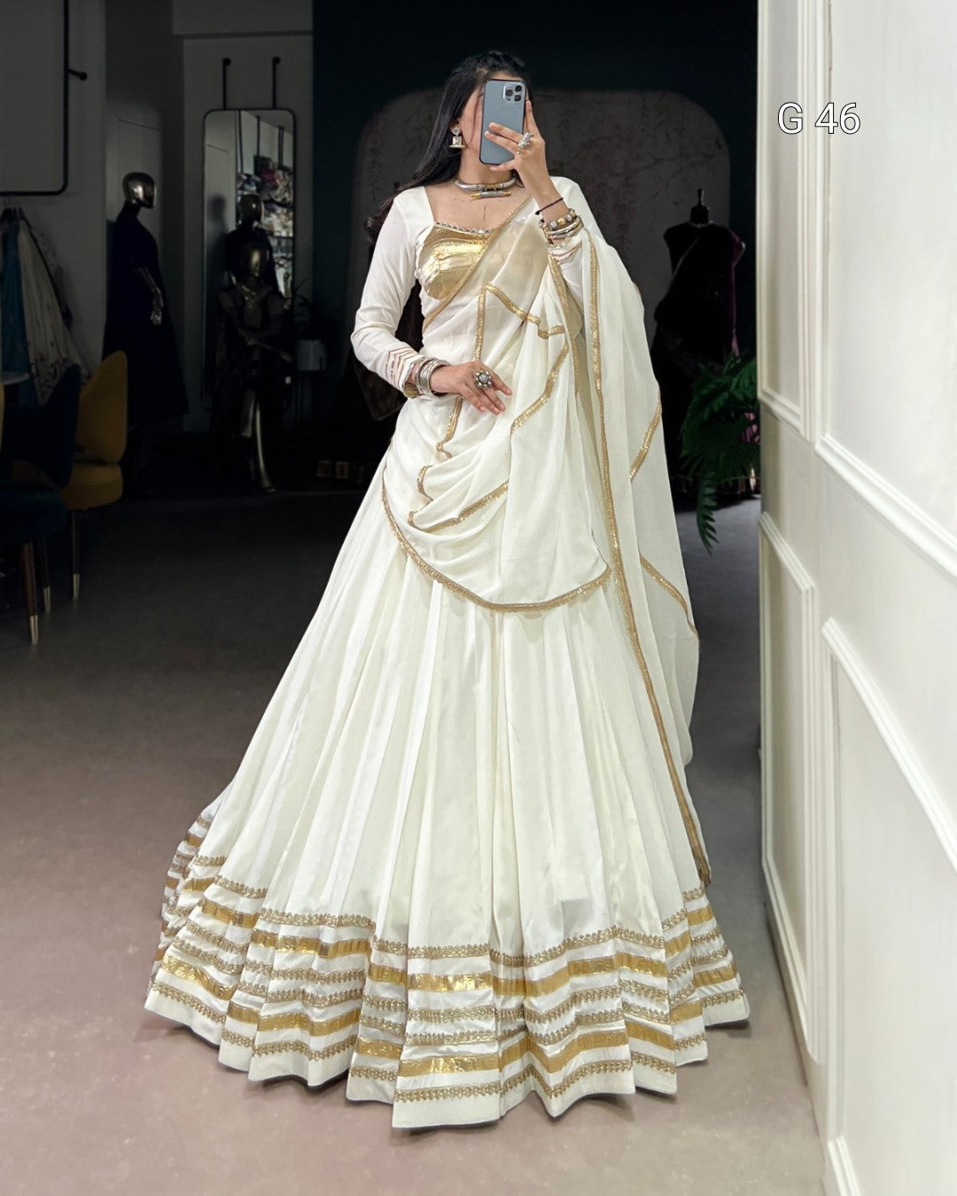 Woman wearing a white and gold saree in an indoor setting.