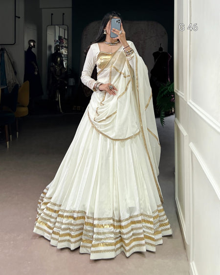 Woman wearing a white and gold saree in an indoor setting.