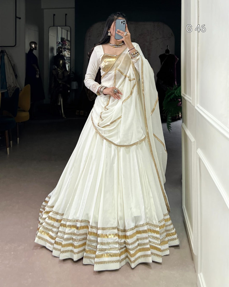 Woman wearing a white and gold saree in an indoor setting.