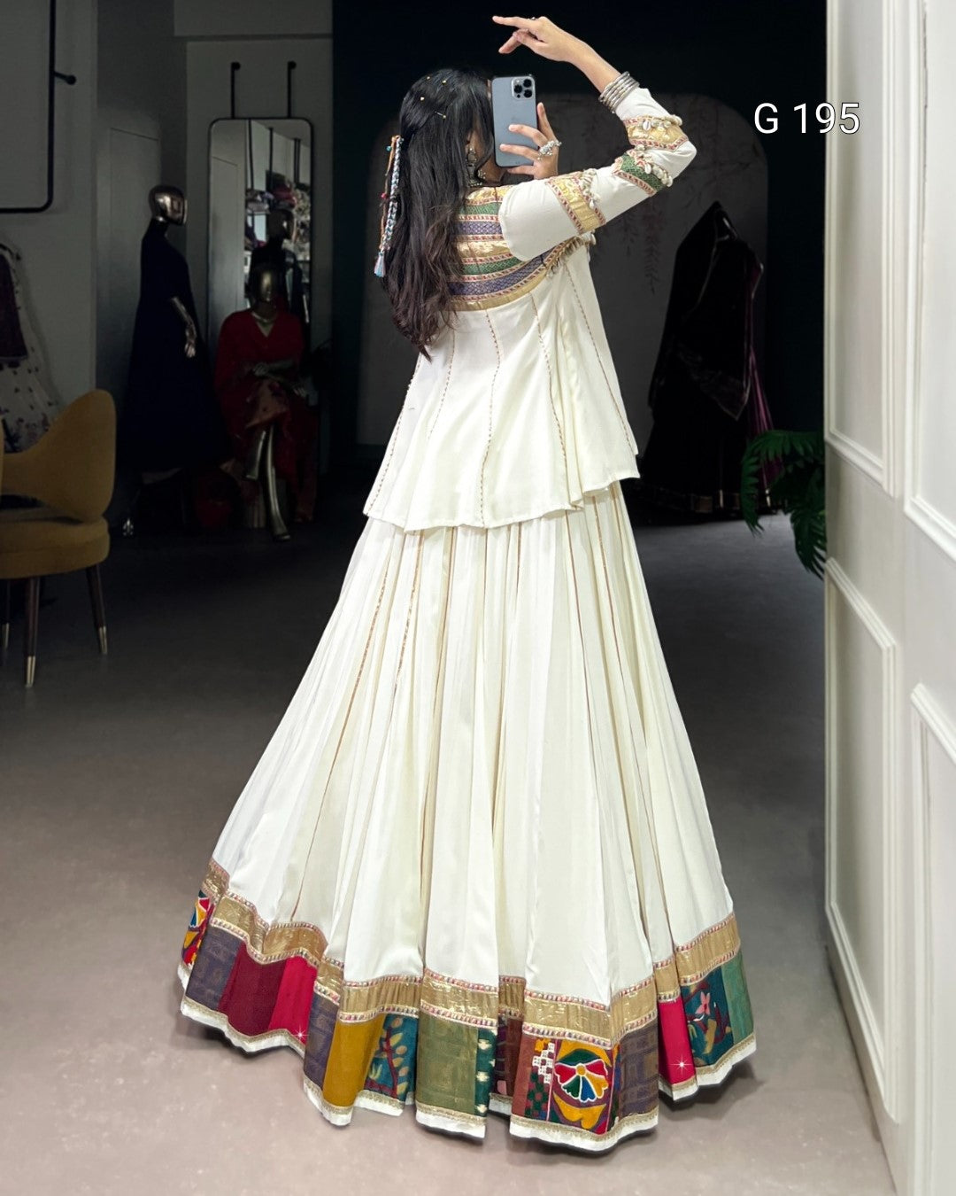 Person wearing a long, white dress with colorful patterns taking a mirror selfie.