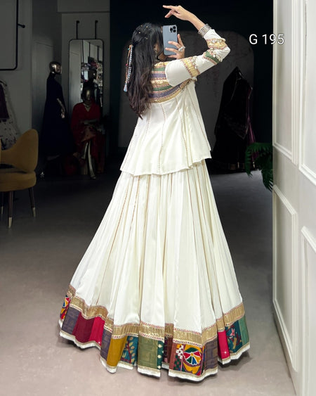 Person wearing a long, white dress with colorful patterns taking a mirror selfie.