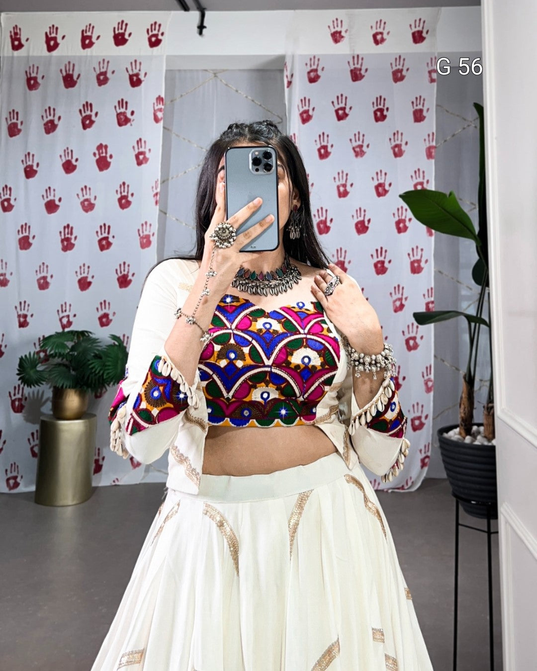 Person wearing a colorful top and white skirt in front of a patterned wall.