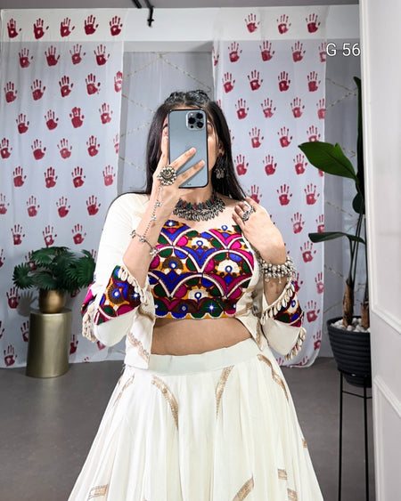 Person wearing a colorful top and white skirt in front of a patterned wall.
