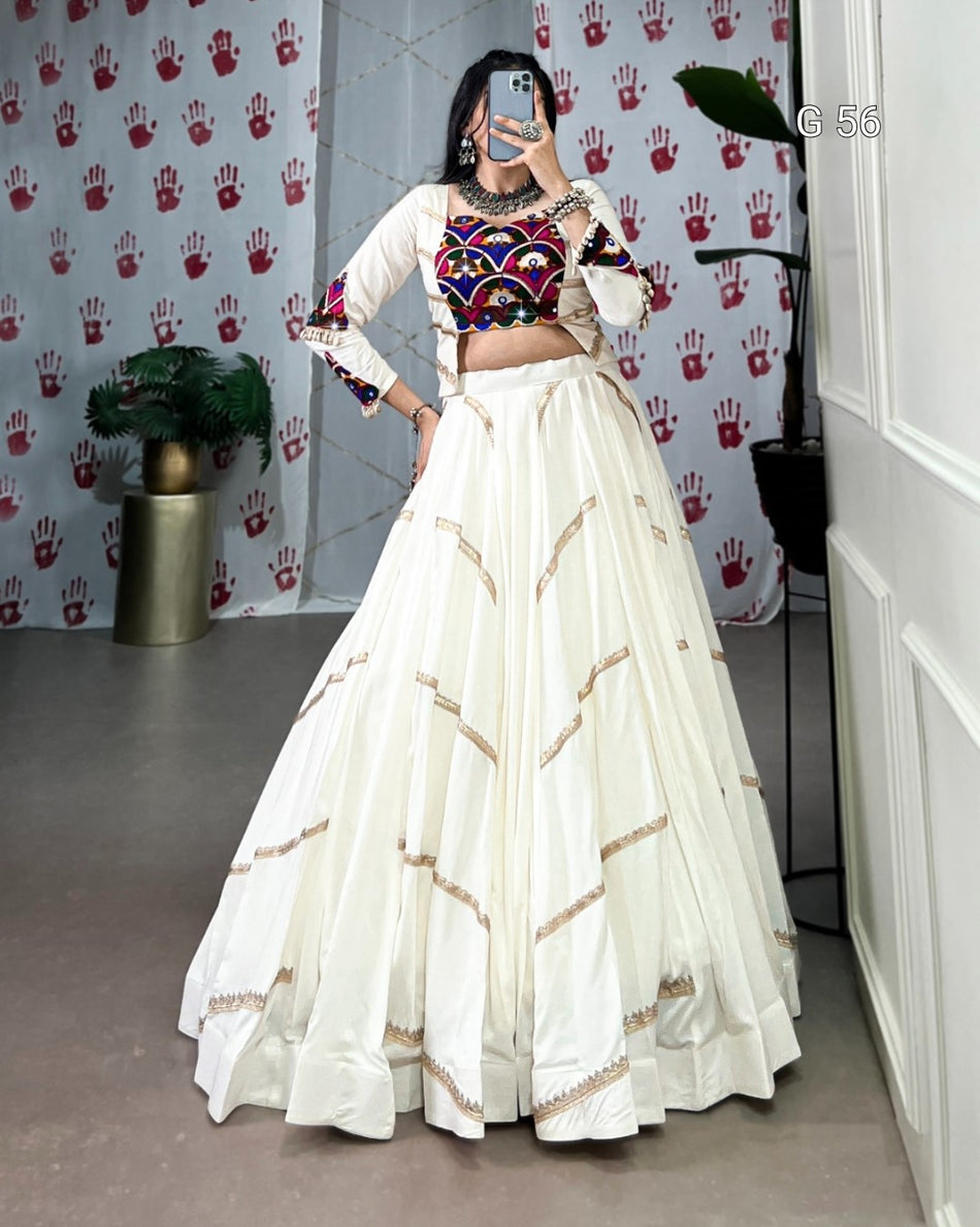 Woman in traditional outfit with colorful top and white skirt in a room with a patterned wall.