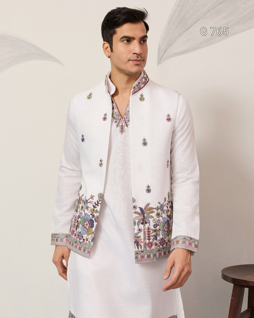 Man wearing a white embroidered jacket over a white kurta against a plain background