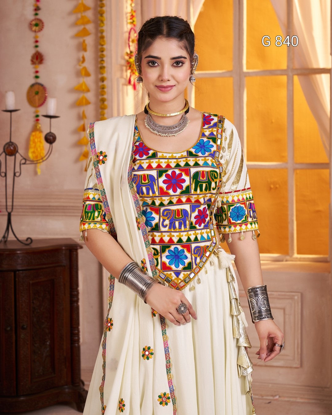 Woman wearing a colorful traditional outfit with intricate patterns in a decorated room.