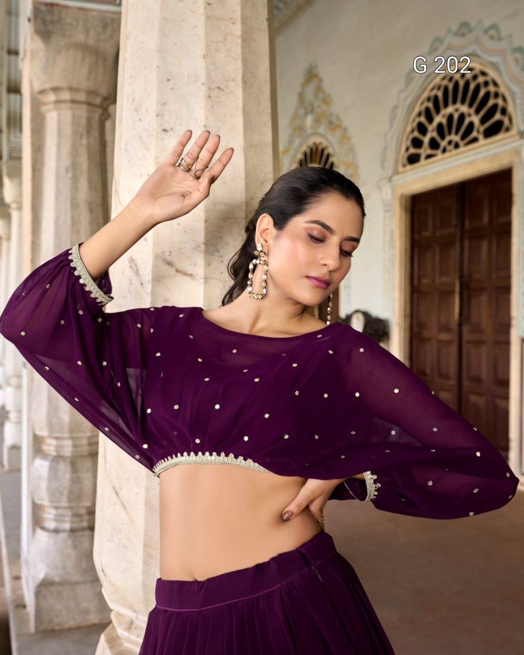 Woman wearing a purple traditional outfit with intricate designs in an outdoor setting.