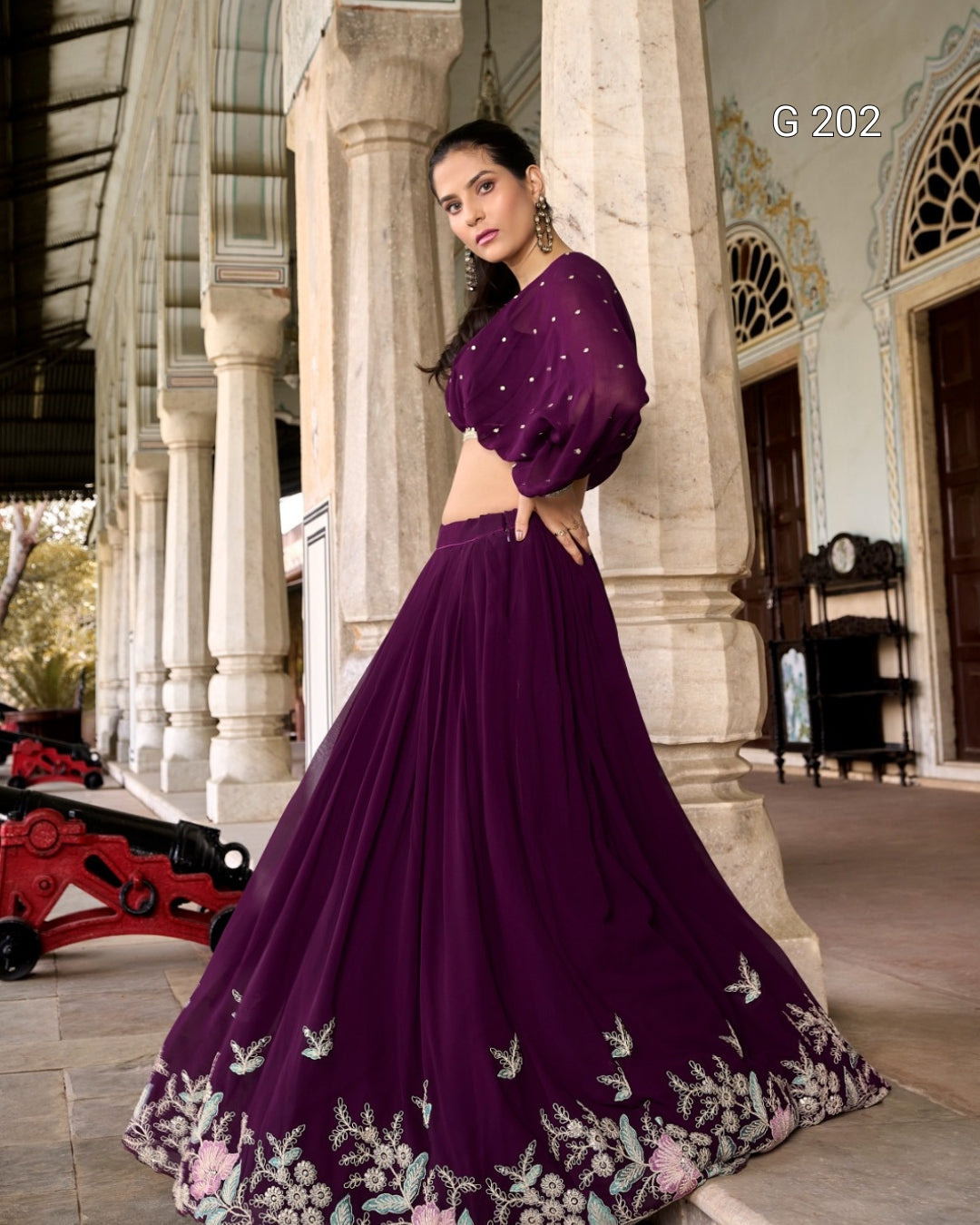 Woman in a purple traditional outfit with floral embroidery standing in an elegant indoor setting.