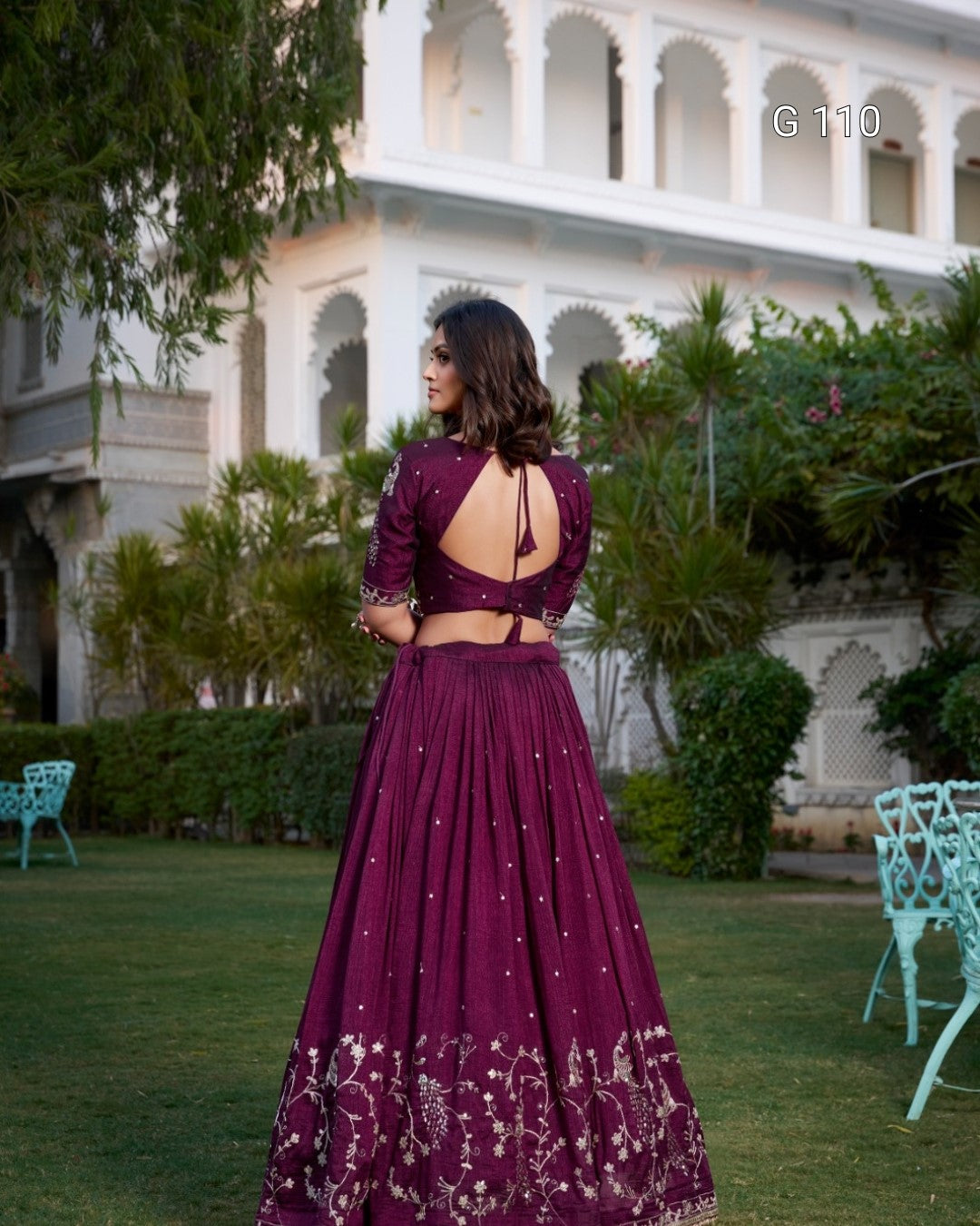 Woman in a purple traditional outfit standing in a garden with a building in the background