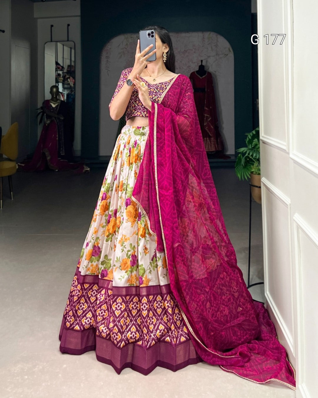 Person wearing a traditional outfit with a floral skirt and pink dupatta in a room.