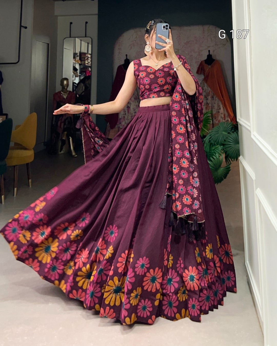 Woman in a purple floral outfit taking a mirror selfie in a room.
