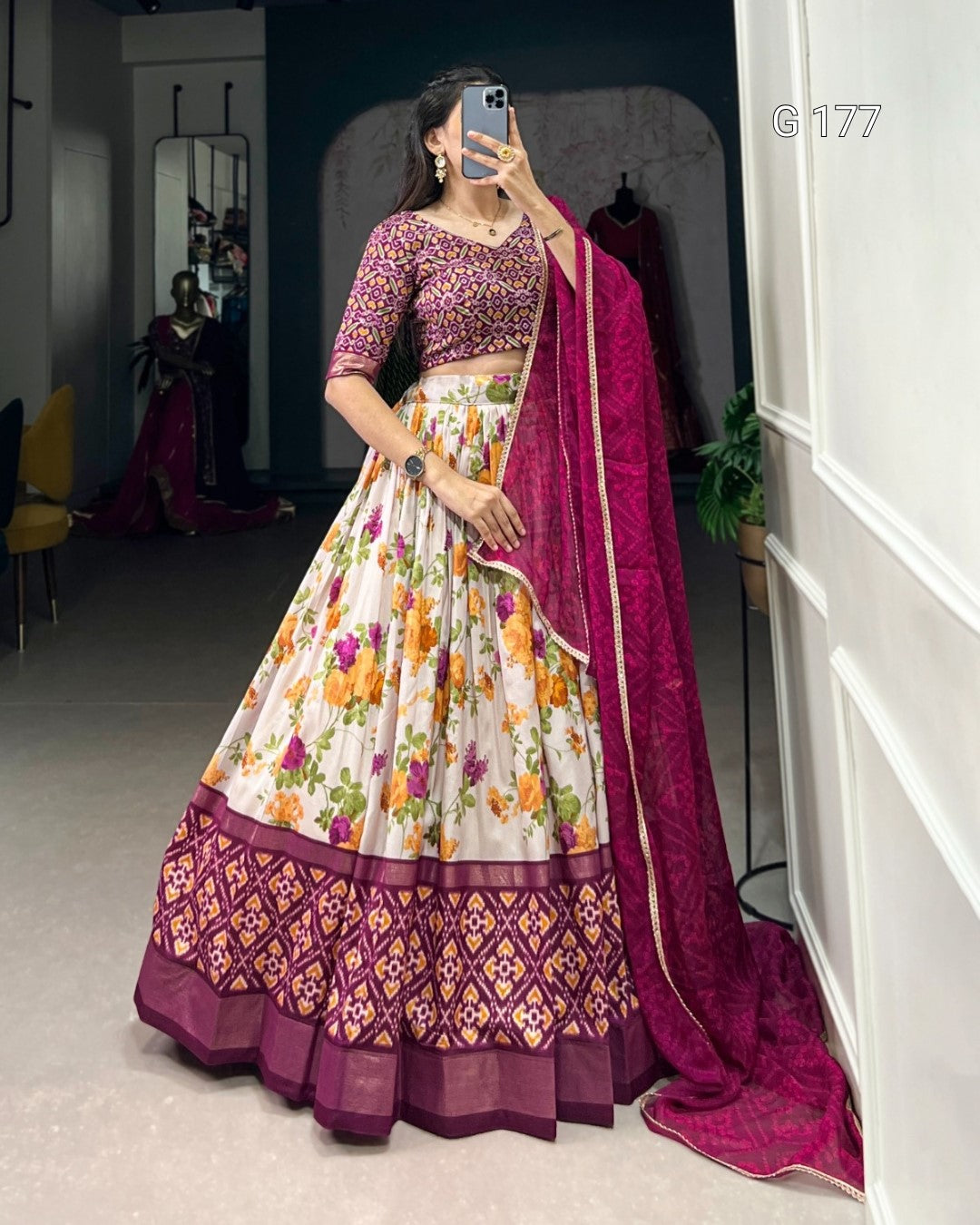 Woman in a traditional outfit with a floral skirt and purple dupatta in a room.