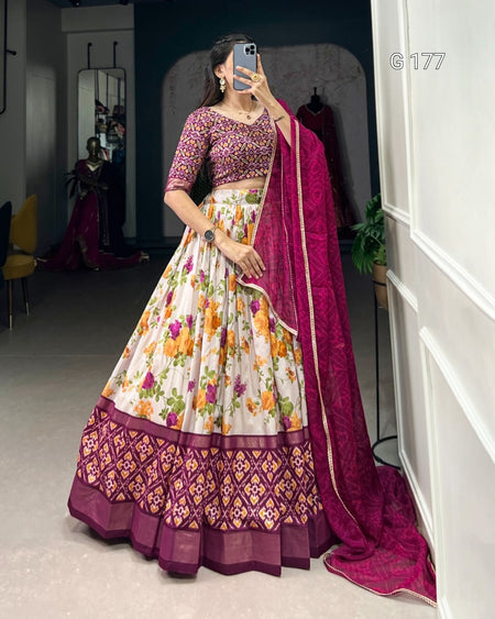 Woman in a traditional outfit with a floral skirt and purple dupatta in a room.