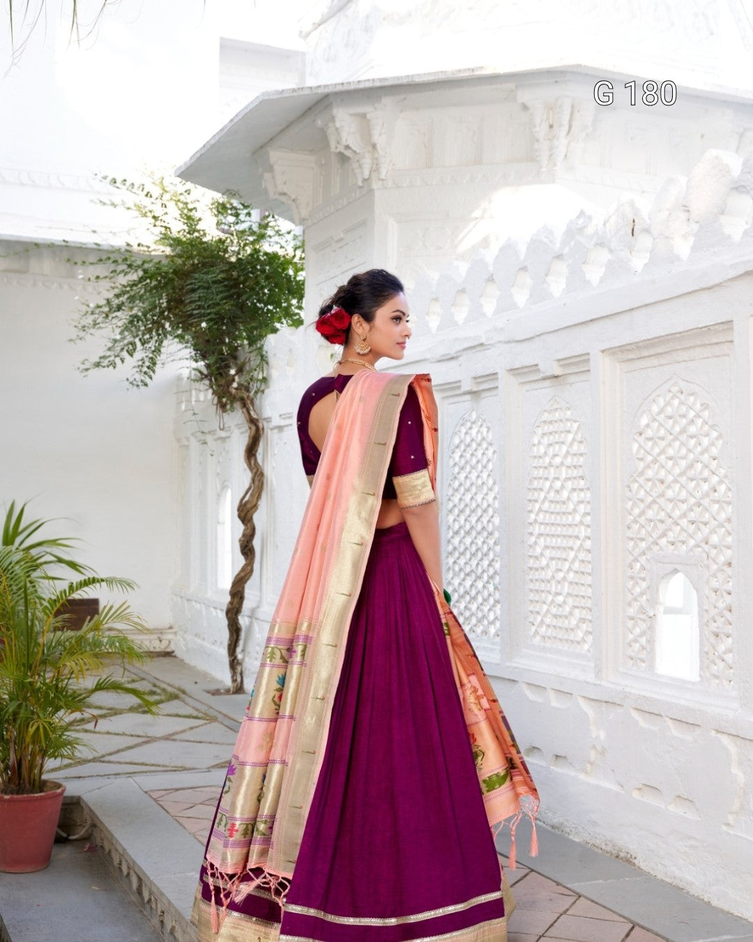Woman in a purple saree with a pink blouse standing in a white architectural setting.