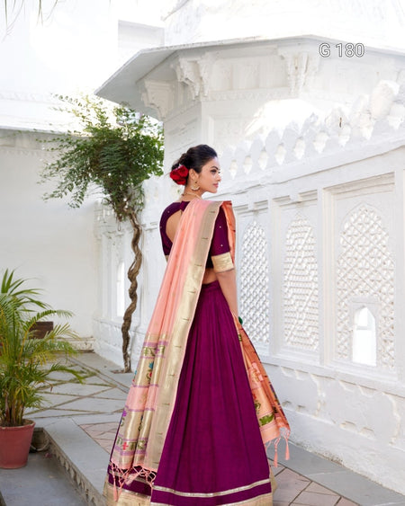 Woman in a purple saree with a pink blouse standing in a white architectural setting.