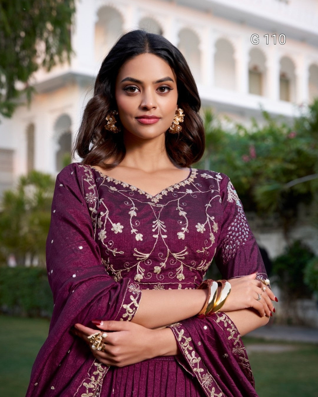 Woman in a purple traditional outfit with floral patterns standing outdoors.