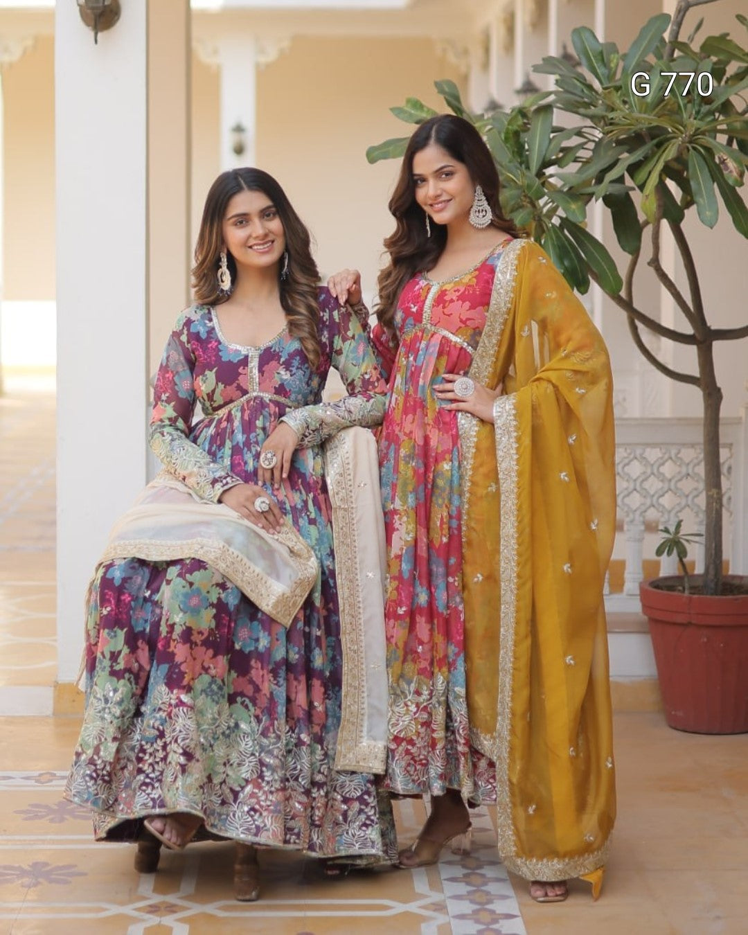 Two women in colorful traditional outfits standing in a decorated indoor setting.