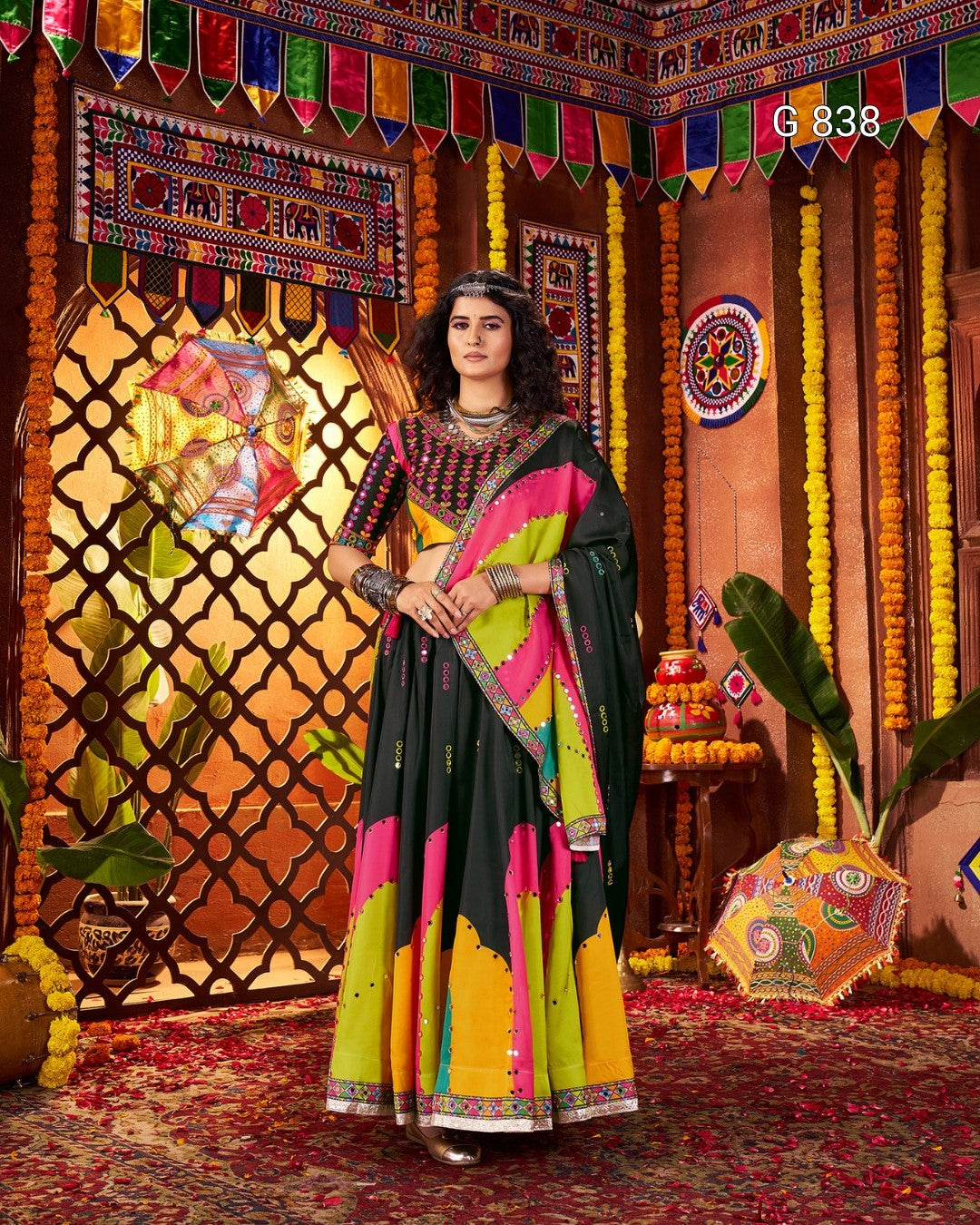 Woman in a colorful traditional outfit standing in front of a decorated wall with vibrant patterns.