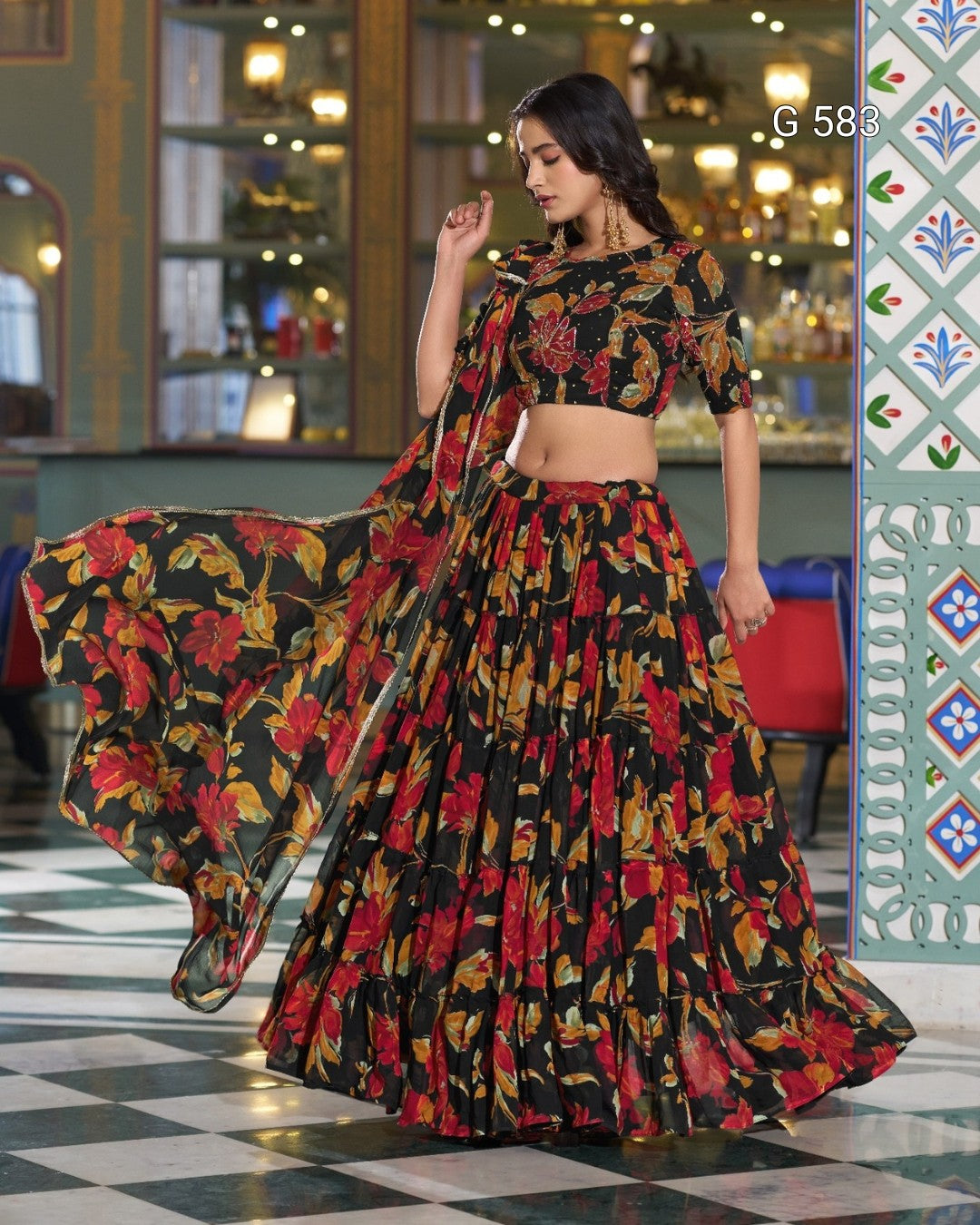 A woman models a black floral print lehenga choli set with a matching dupatta in an ornate indoor setting. The outfit features a red, yellow, and orange floral pattern on a black background.