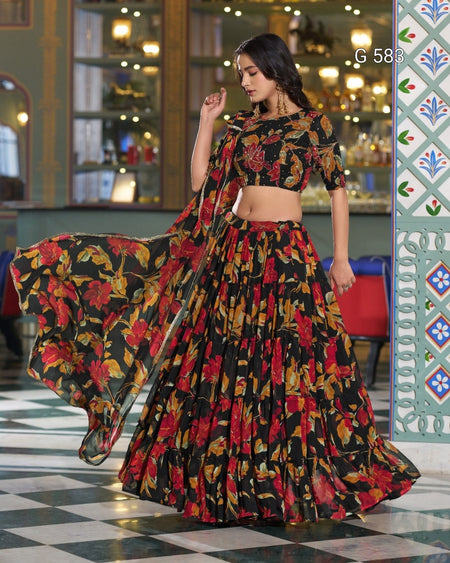 A woman models a black floral print lehenga choli set with a matching dupatta in an ornate indoor setting. The outfit features a red, yellow, and orange floral pattern on a black background.