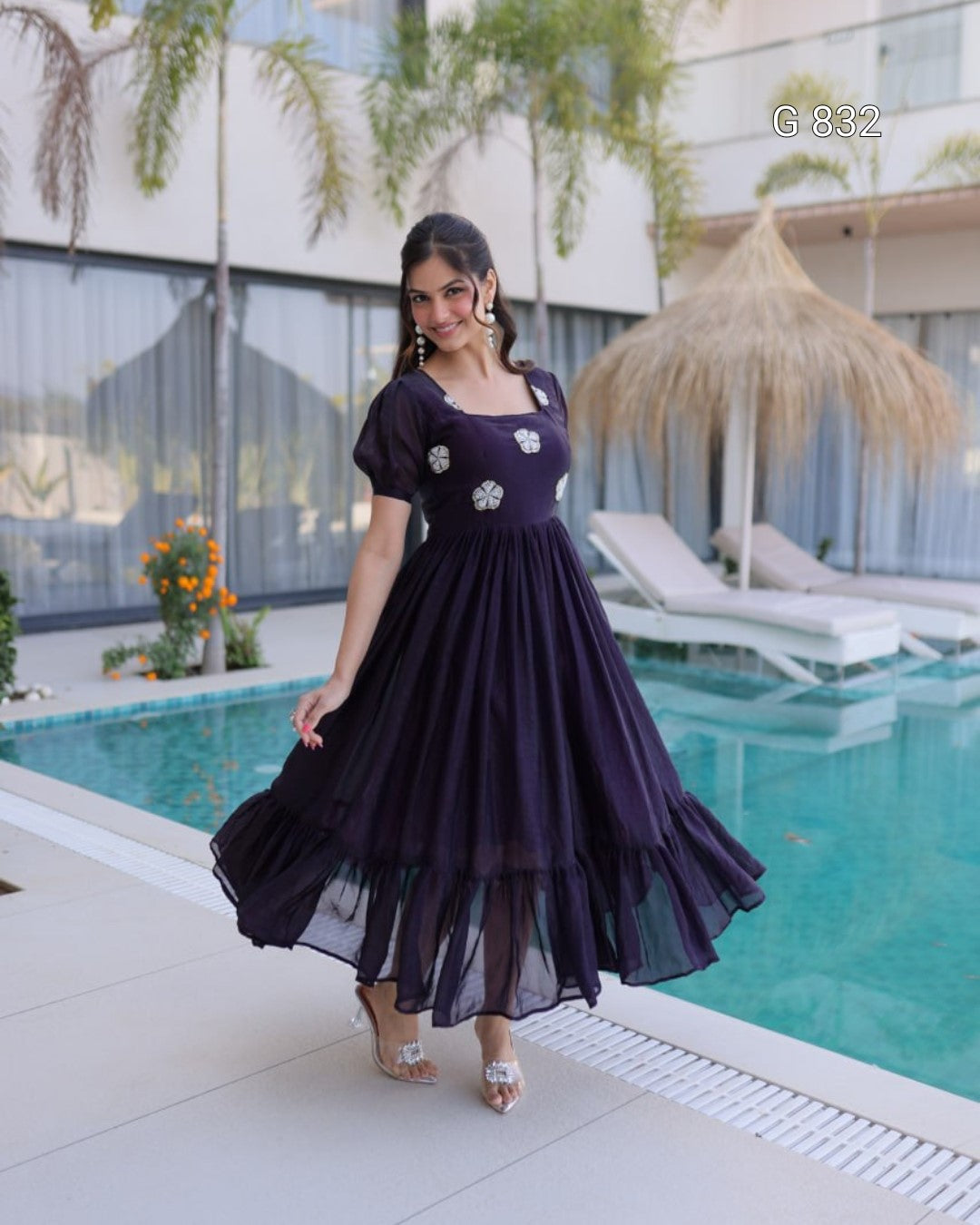 Woman in a purple dress standing by a pool with a building and plants in the background