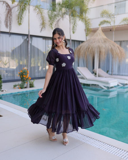 Woman in a purple dress standing by a pool with a building and plants in the background