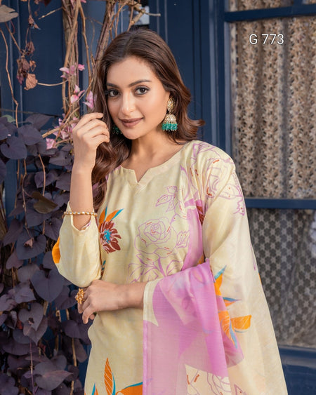 Woman wearing a floral dress with a pink dupatta, standing against a decorative wall.