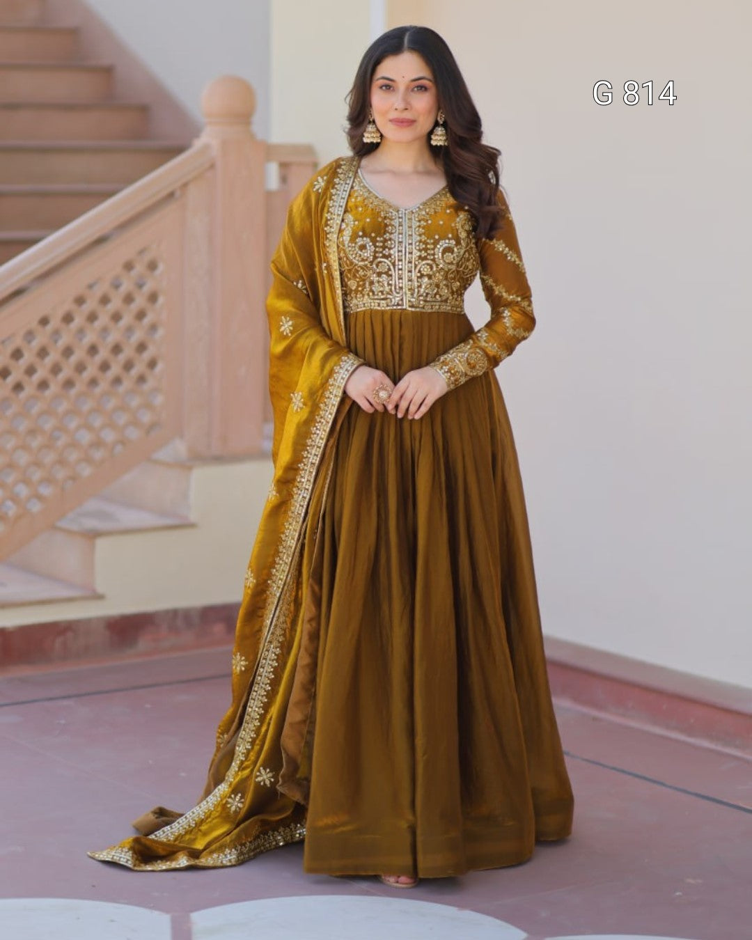 Woman in a traditional outfit with gold and brown colors standing in a decorative interior setting.