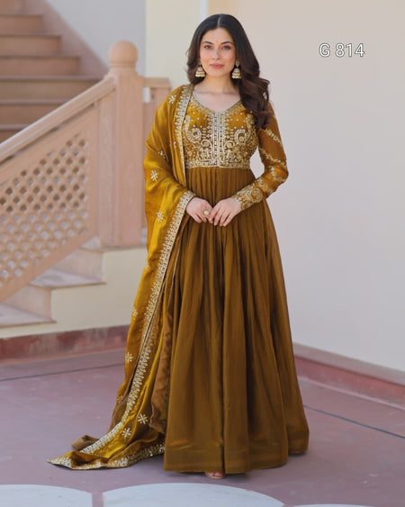 Woman in a traditional outfit with gold and brown colors standing in a decorative interior setting.
