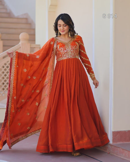 Woman wearing an orange traditional outfit with gold embroidery indoors.