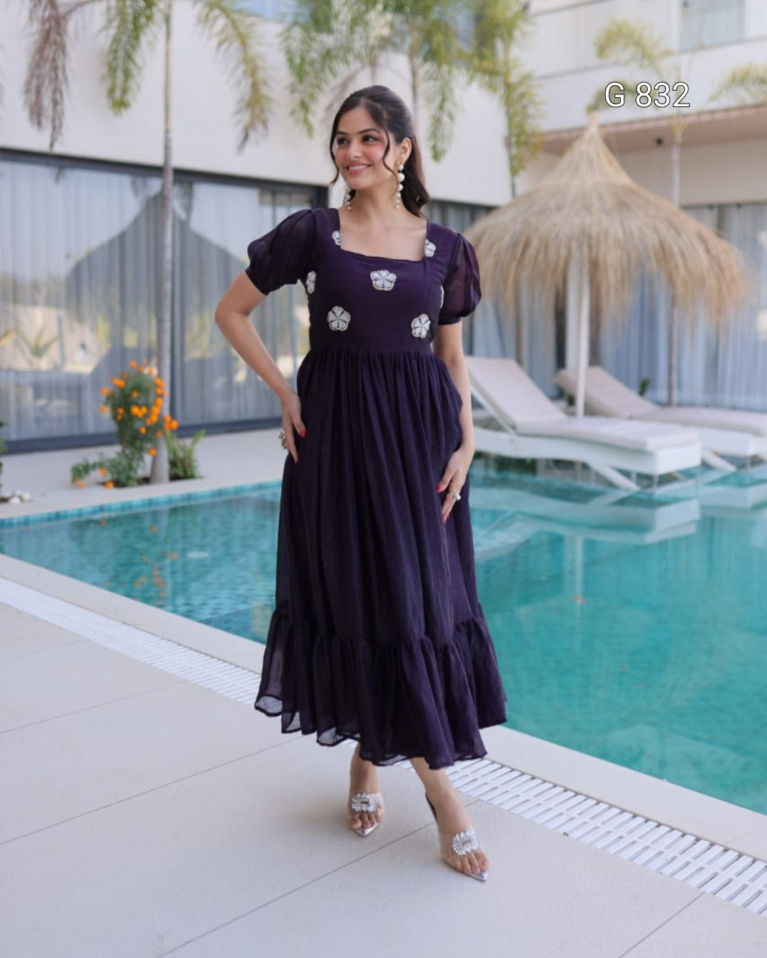 Woman in a dark purple dress standing by a poolside.