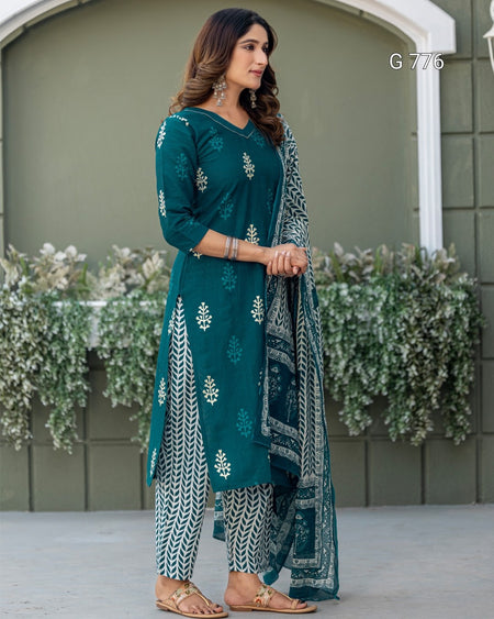 Woman wearing a teal traditional outfit with white patterns in front of a green wall.