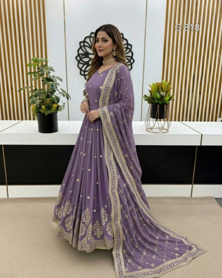 Woman in a purple embroidered saree standing indoors with decorative elements.