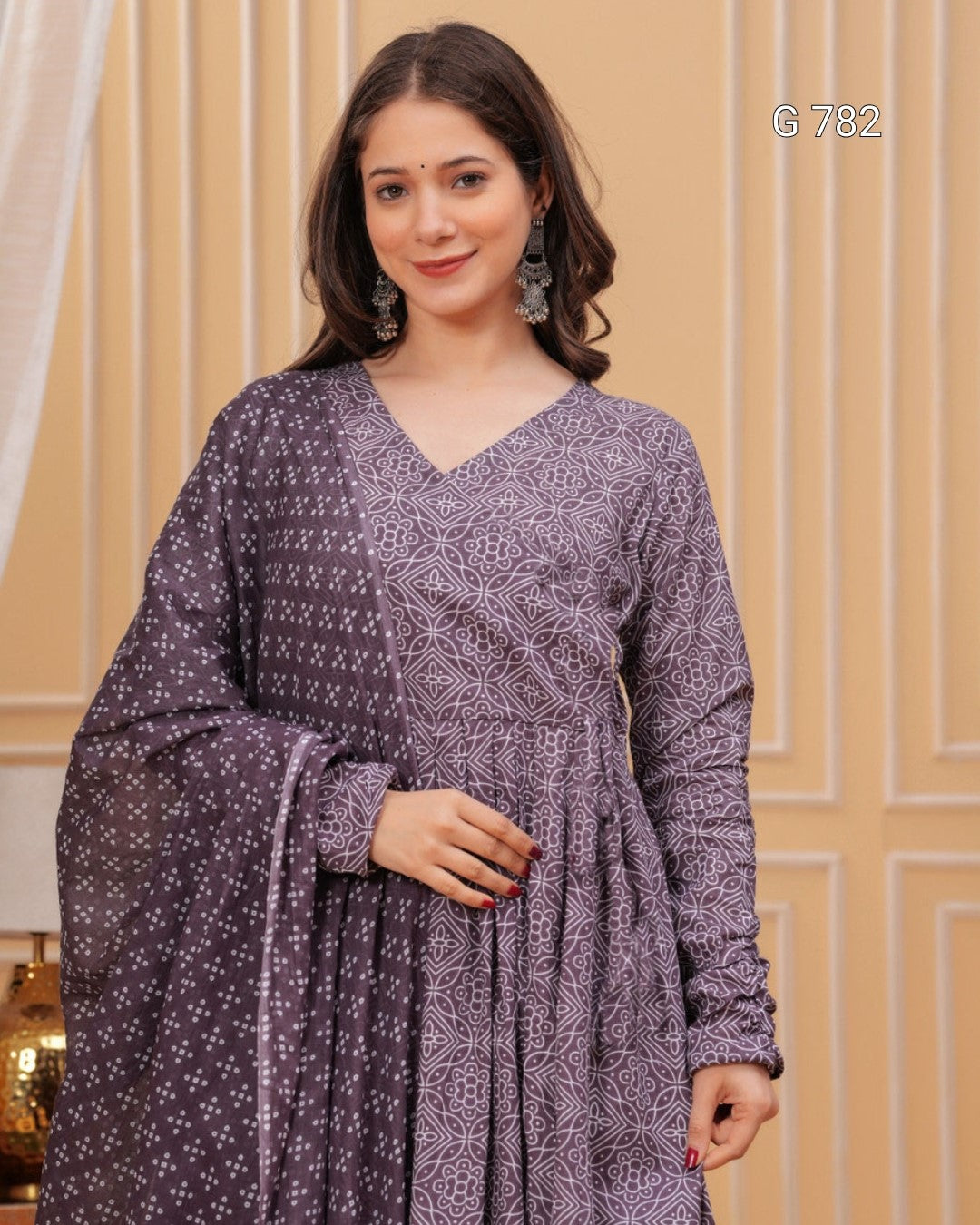 Woman wearing a purple patterned dress against a beige wall.