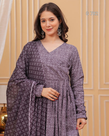 Woman wearing a purple patterned dress against a beige wall.