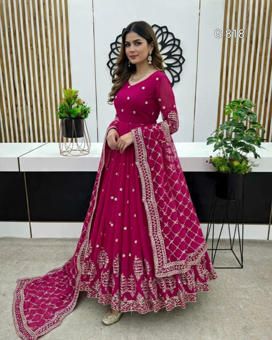 Woman in a pink traditional outfit with intricate designs standing indoors.