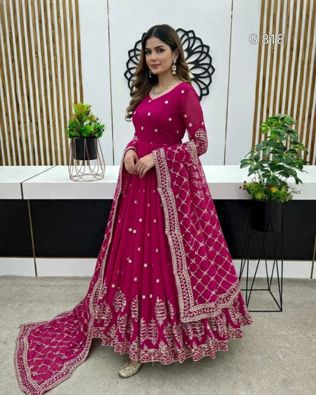 Woman in a pink traditional outfit with intricate designs standing indoors.