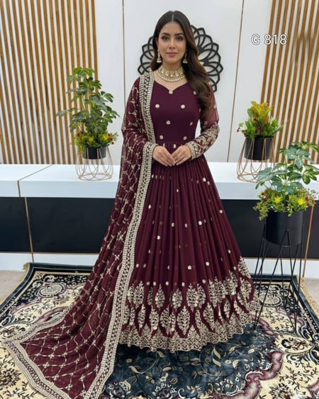 Woman in a maroon traditional outfit with gold embroidery standing in a decorated room.