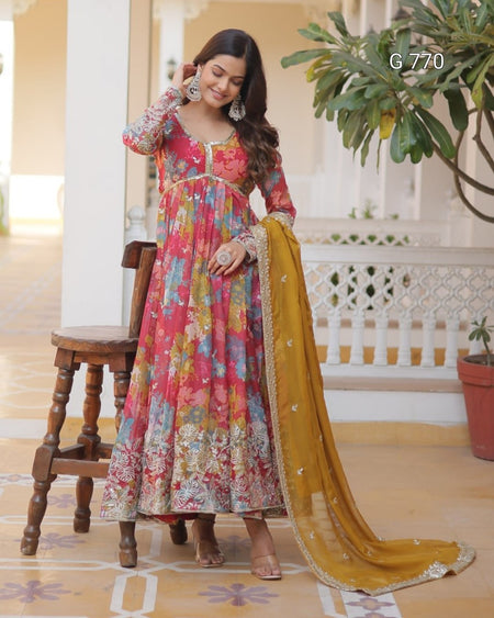 Woman in a colorful floral dress with a yellow dupatta standing indoors.