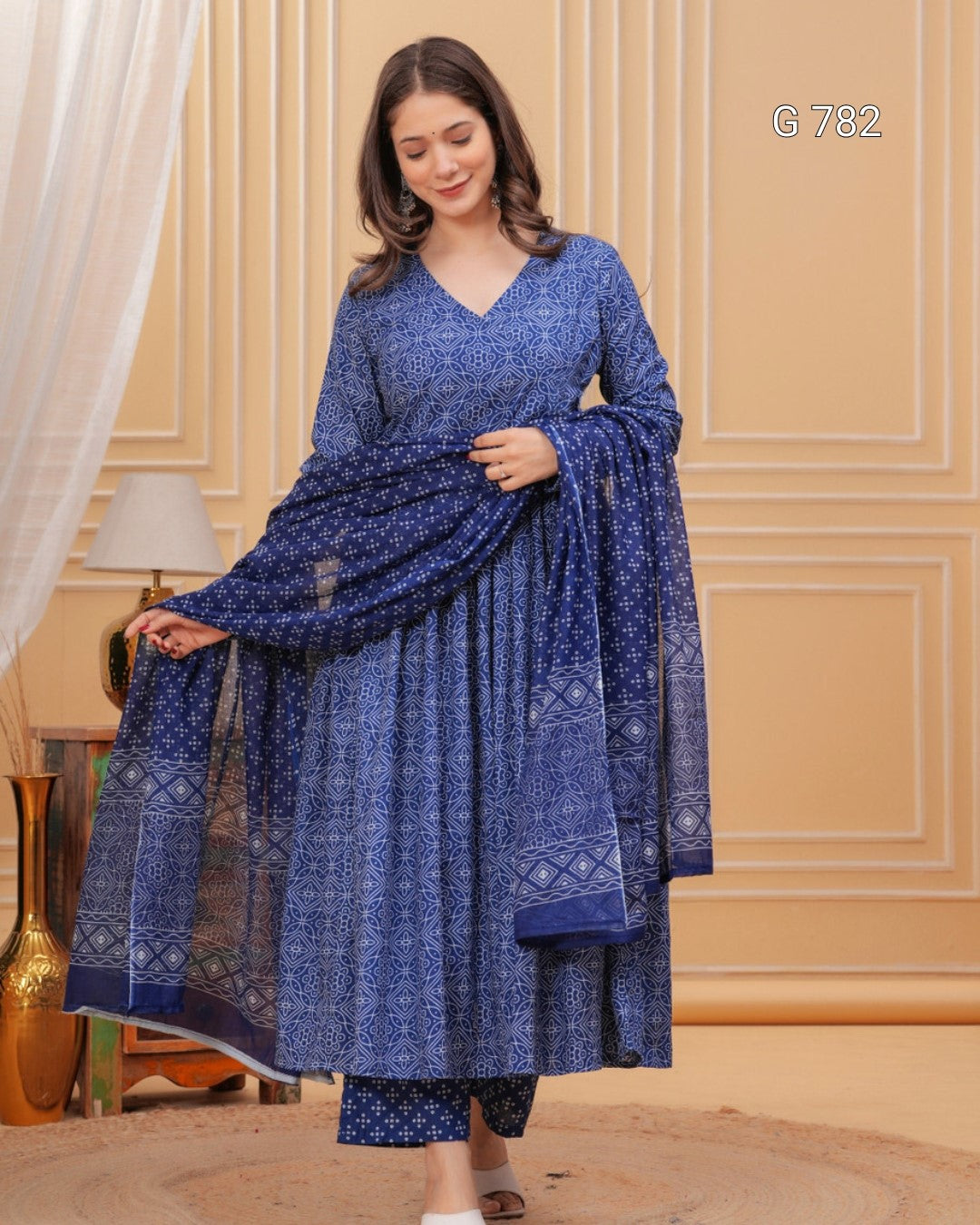 Woman wearing a blue patterned dress with a matching dupatta in a room with beige walls.