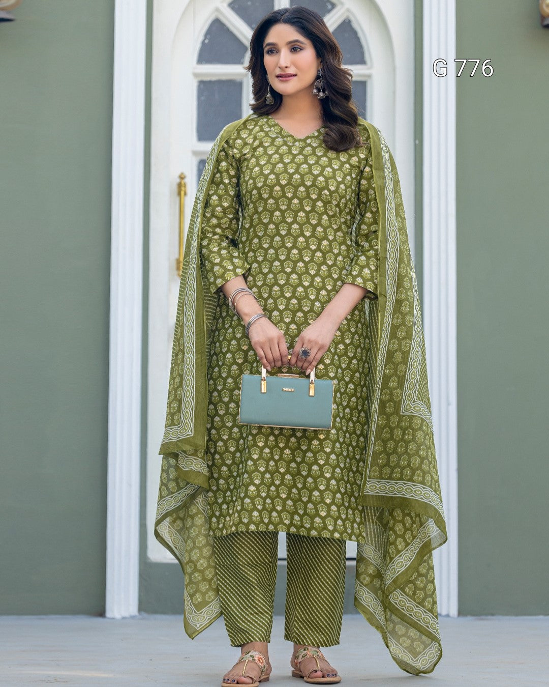 Woman wearing a green patterned outfit with a matching dupatta, holding a light blue handbag.