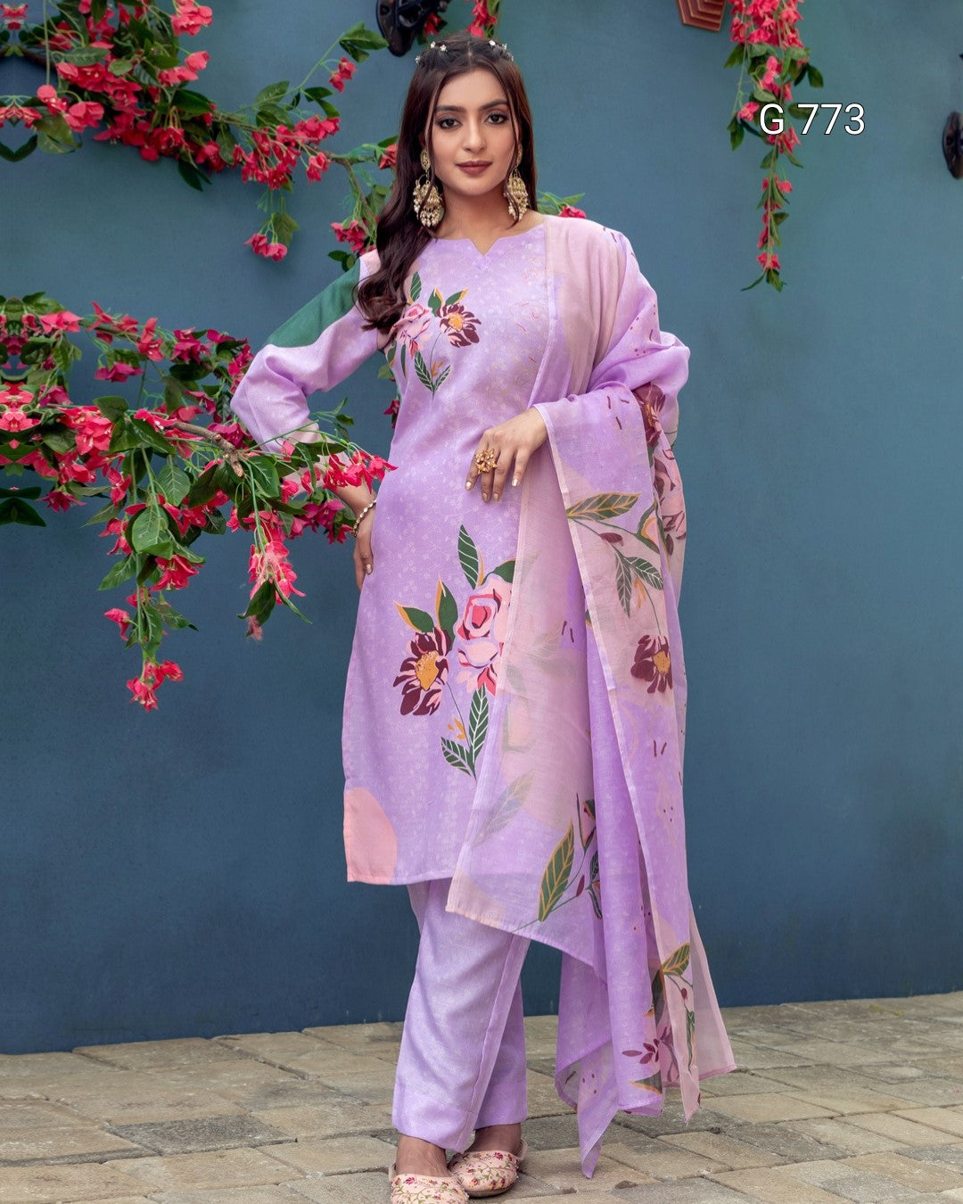 Woman wearing a light purple traditional outfit with floral patterns against a blue wall with pink flowers.