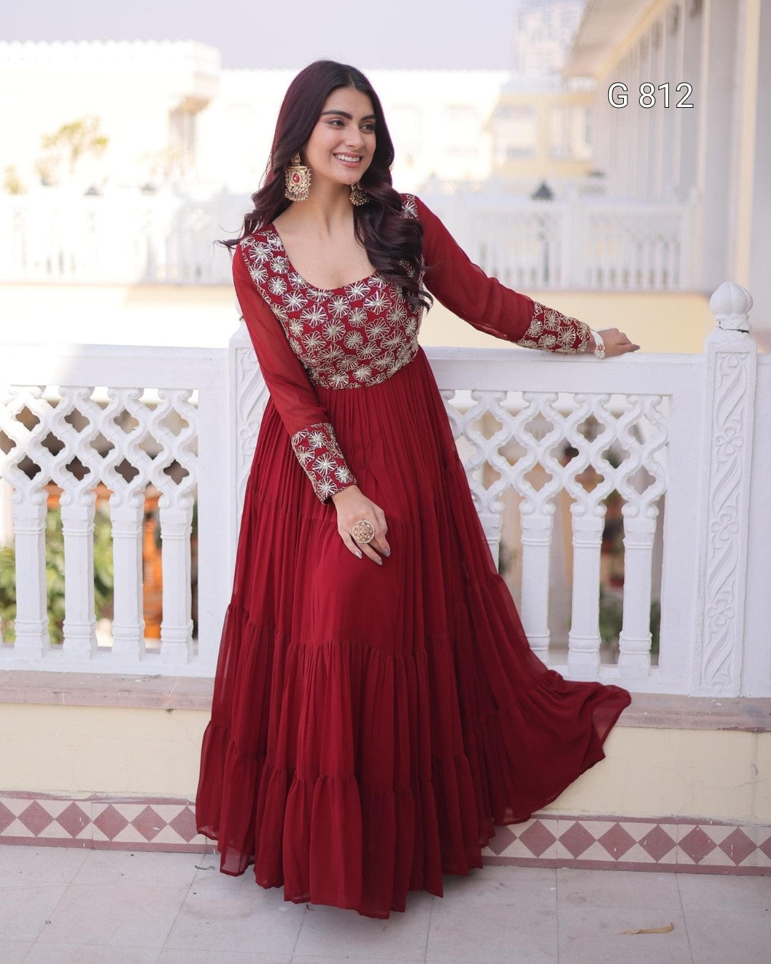 Woman in a red traditional outfit with floral patterns standing on a balcony.