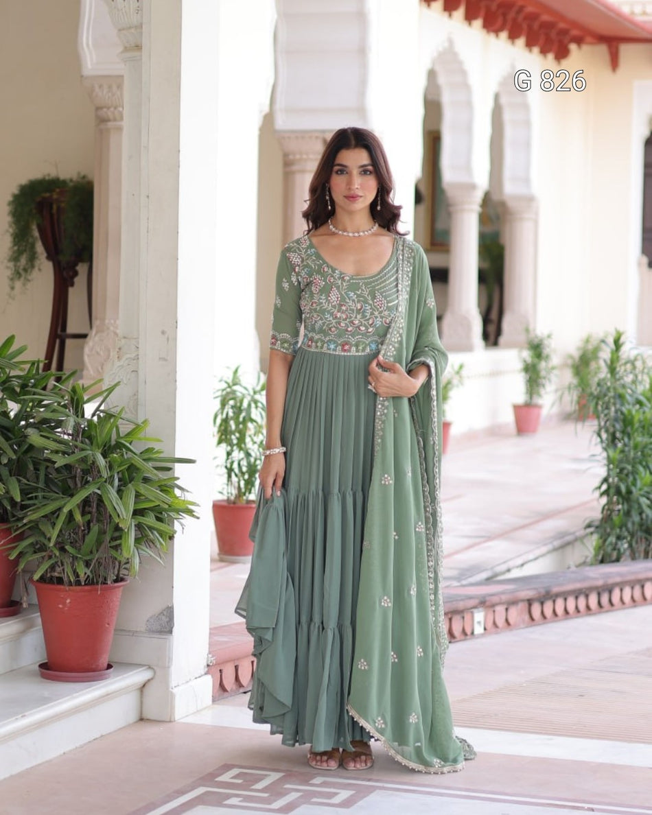 Woman in a green traditional outfit standing in a decorative outdoor setting with plants and architectural elements.