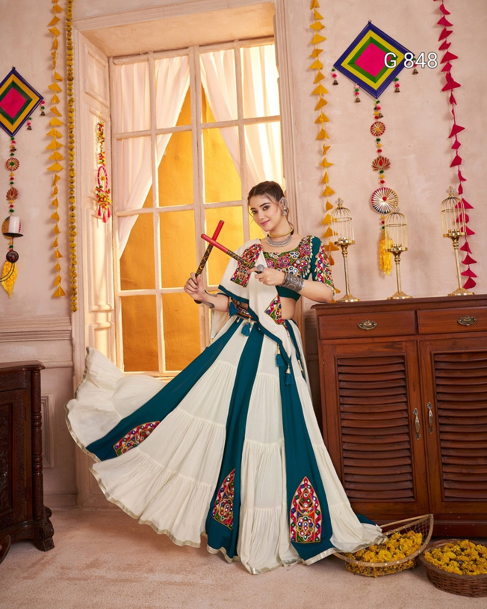 Woman in traditional attire standing in a decorated room with a window and decorative items.