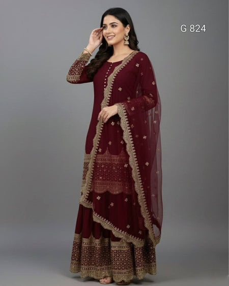 Woman wearing a maroon traditional outfit with gold embroidery on a gray background