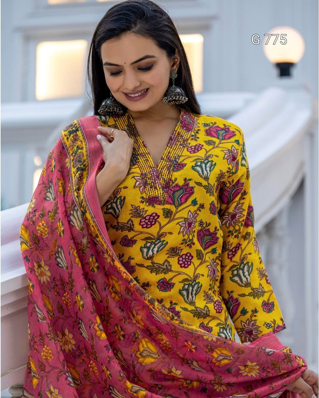 Woman wearing a yellow floral dress with a pink dupatta in an indoor setting