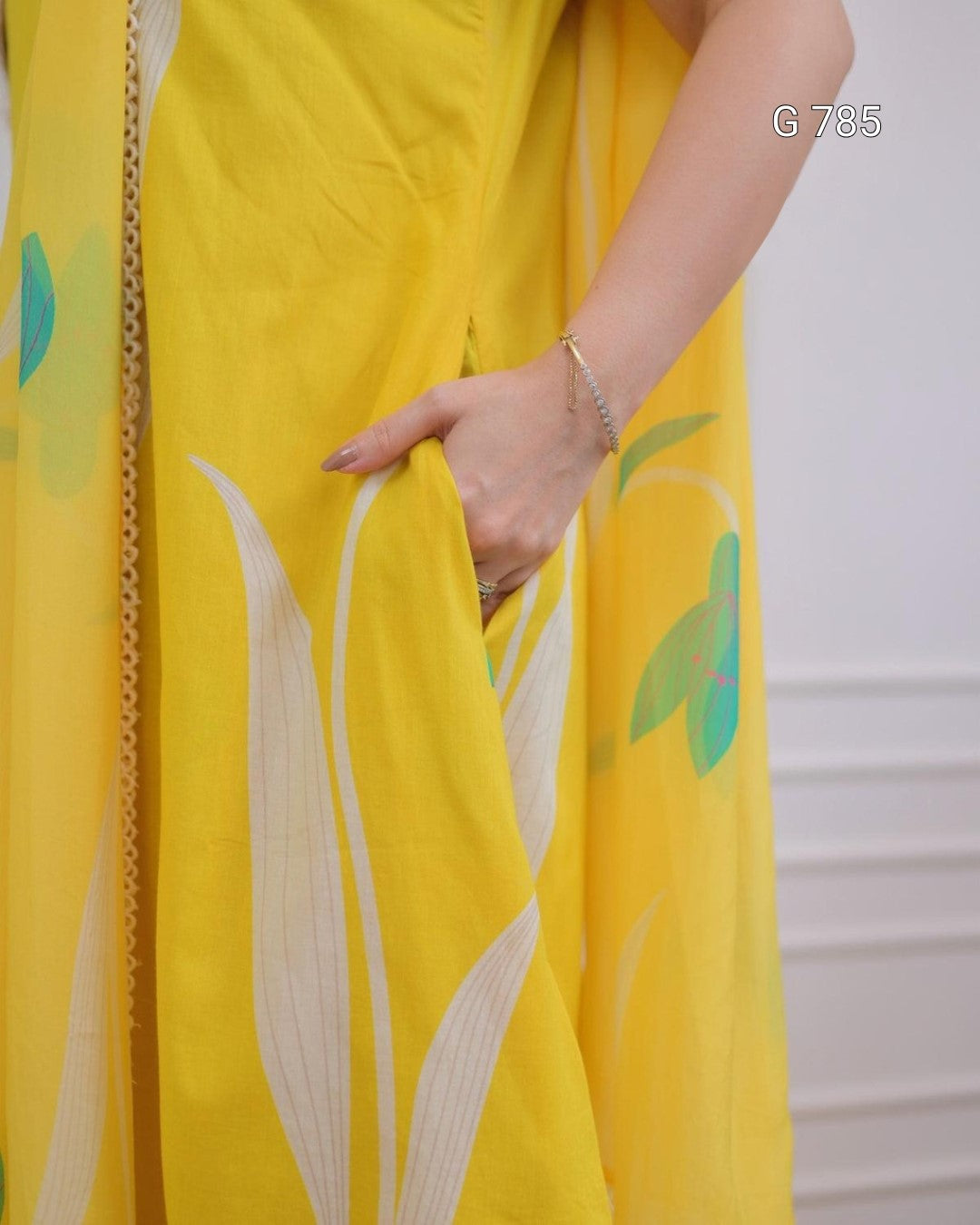 Yellow garment with leaf patterns and a hand touching it against a neutral background